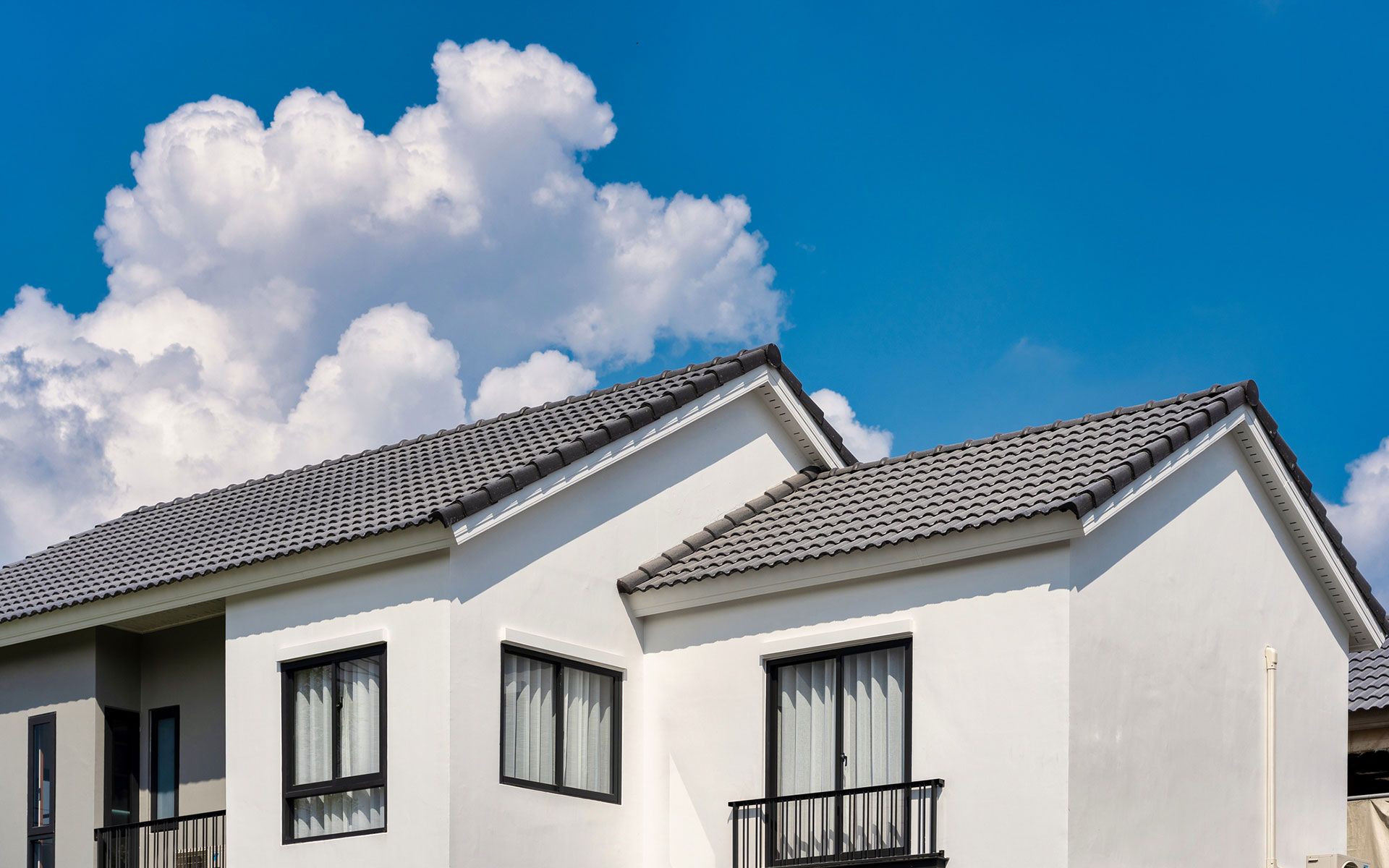 A white house with a tiled roof is against a blue sky with clouds.