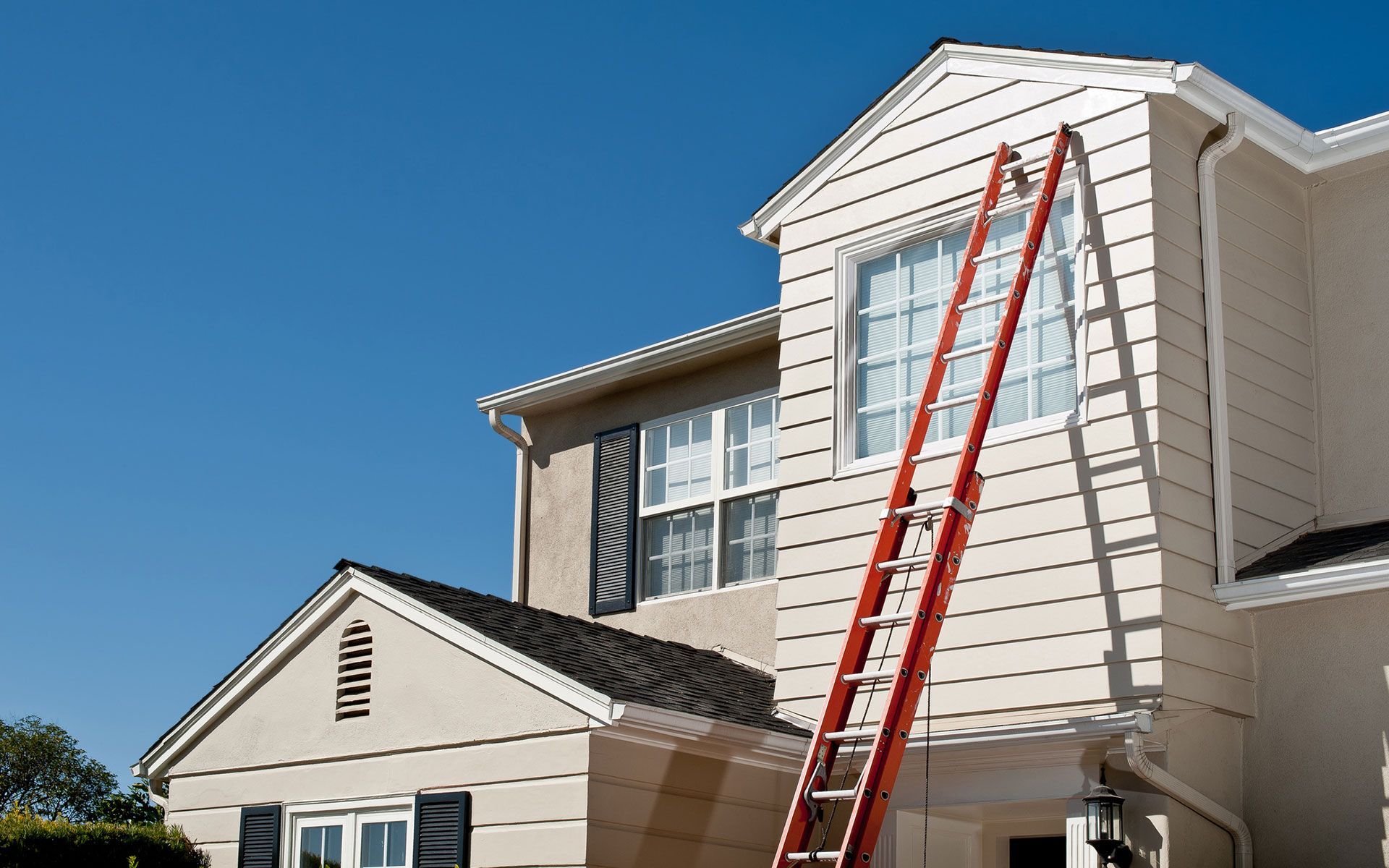 A house is being painted with a red ladder attached to it.
