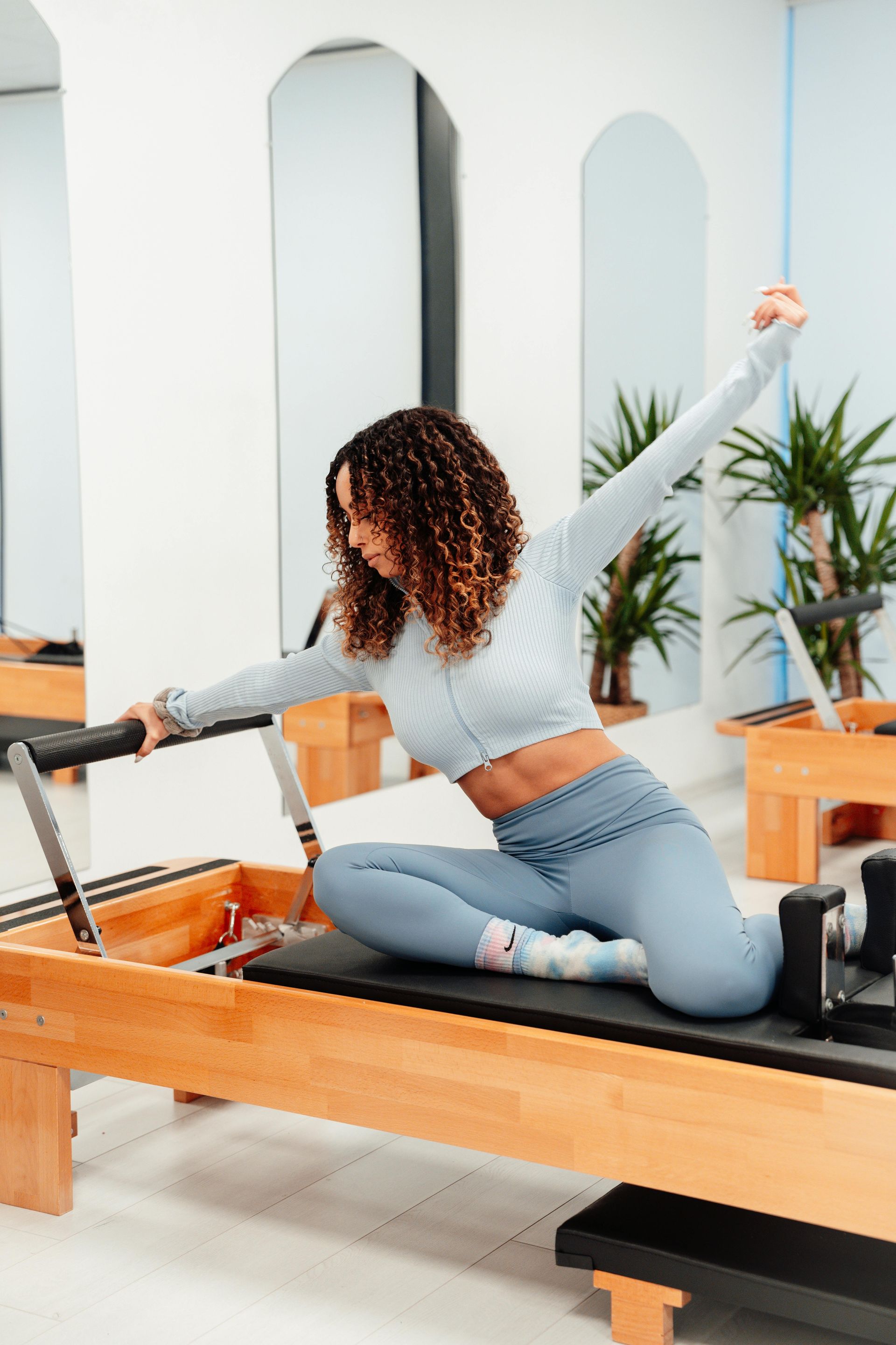 A woman is sitting on a pilates machine with her arms outstretched.