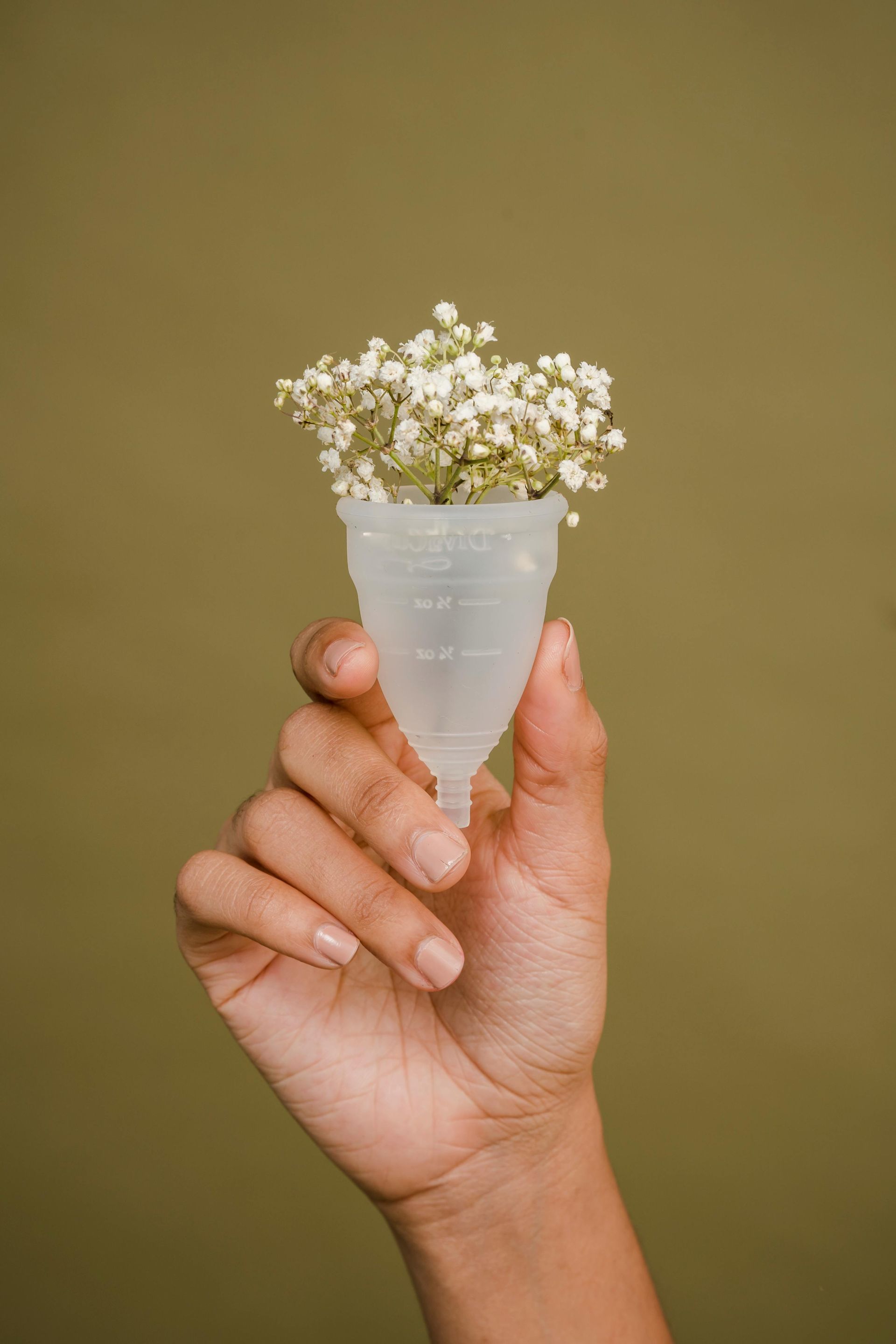 Hand holding menstrual cup filled with white flowers, against a green background.