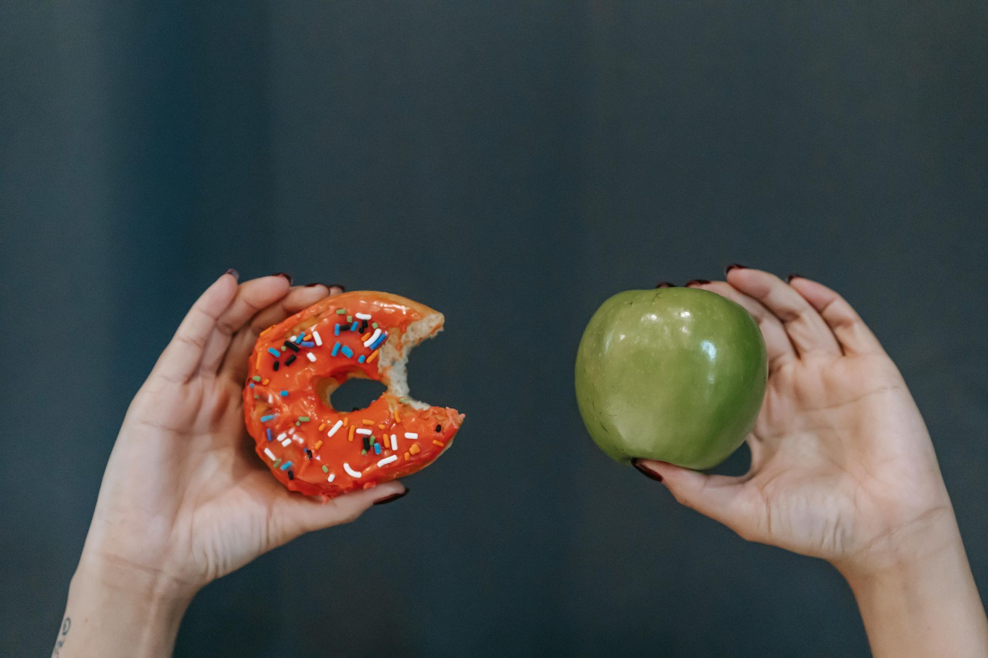 A person is holding a donut and an apple in their hands.