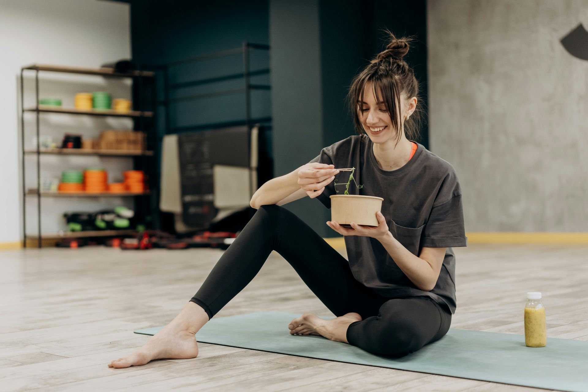 A woman is sitting on a yoga mat eating food.