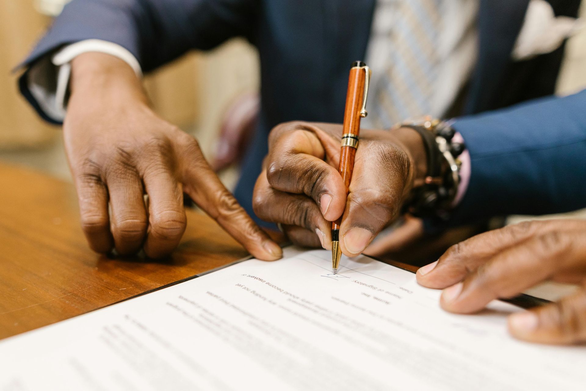 Hands focus on a document as a pen is used to sign a contract, with a finger pointing to a specific section.