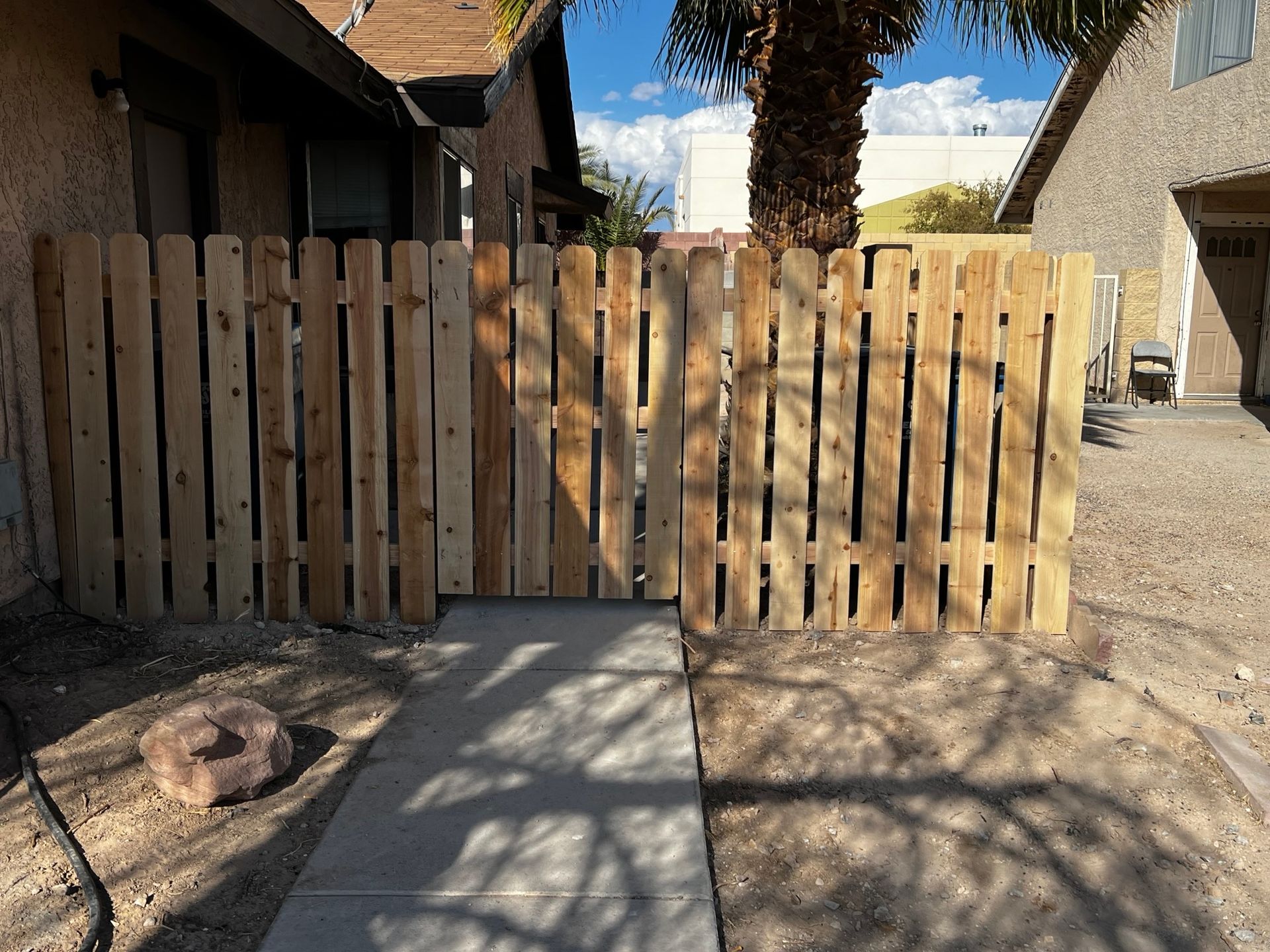 Person installing a wooden fence. They are wearing a hat, grey shirt, and jeans, and working outdoors.