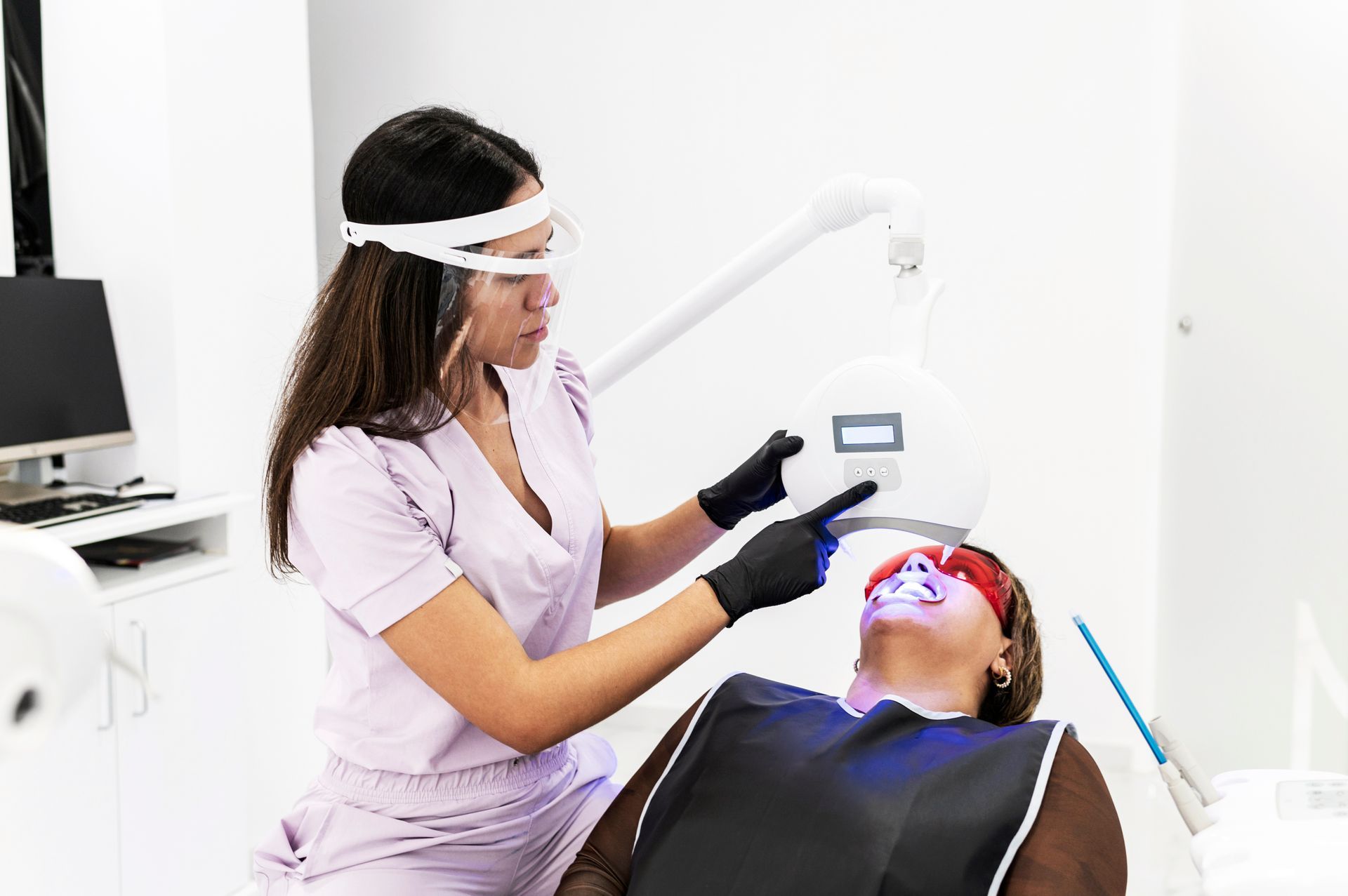 Professional teeth whitening treatments by dentist using LED light on patient in clinic chair.