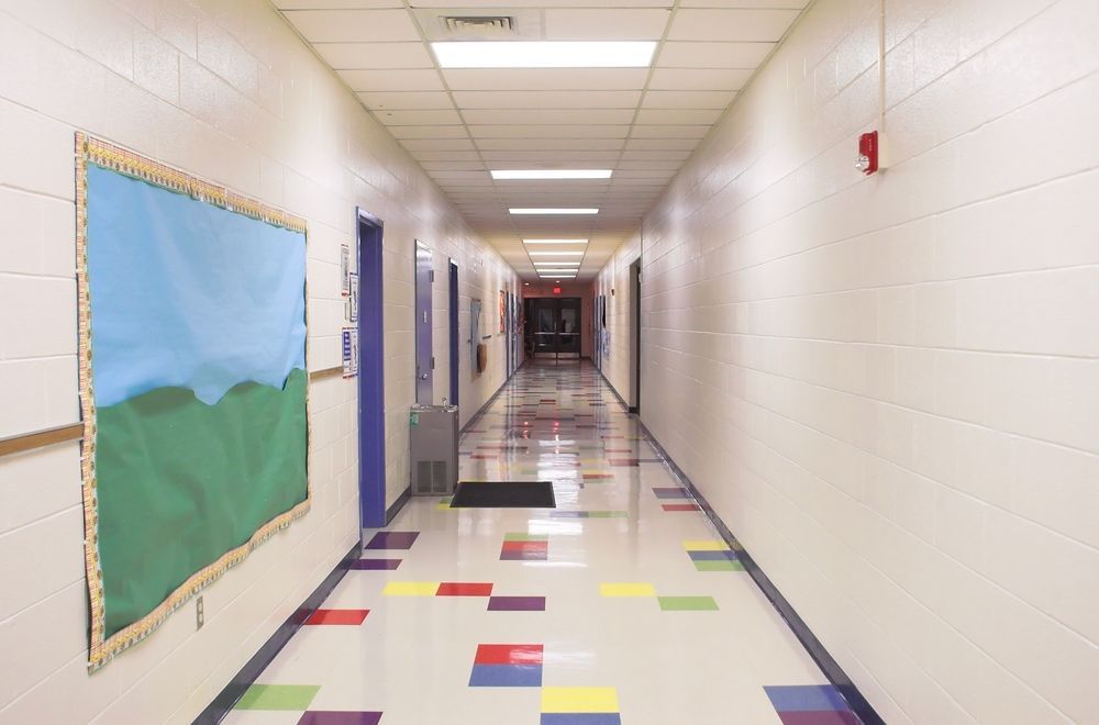 A long hallway in a school with a bulletin board on the wall.