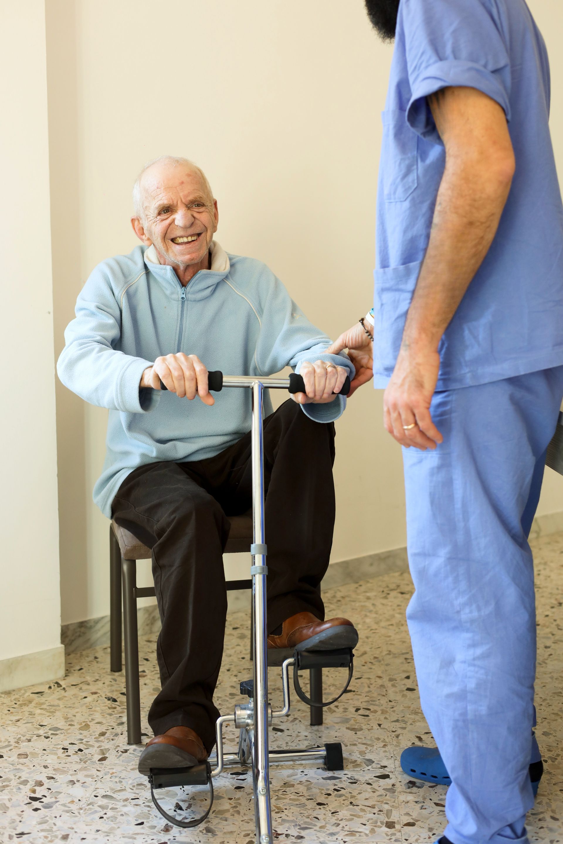 Un gruppo di anziani seduti a un tavolo con degli assistenti. Un assistente mette una mano sulla spalla di un anziano.