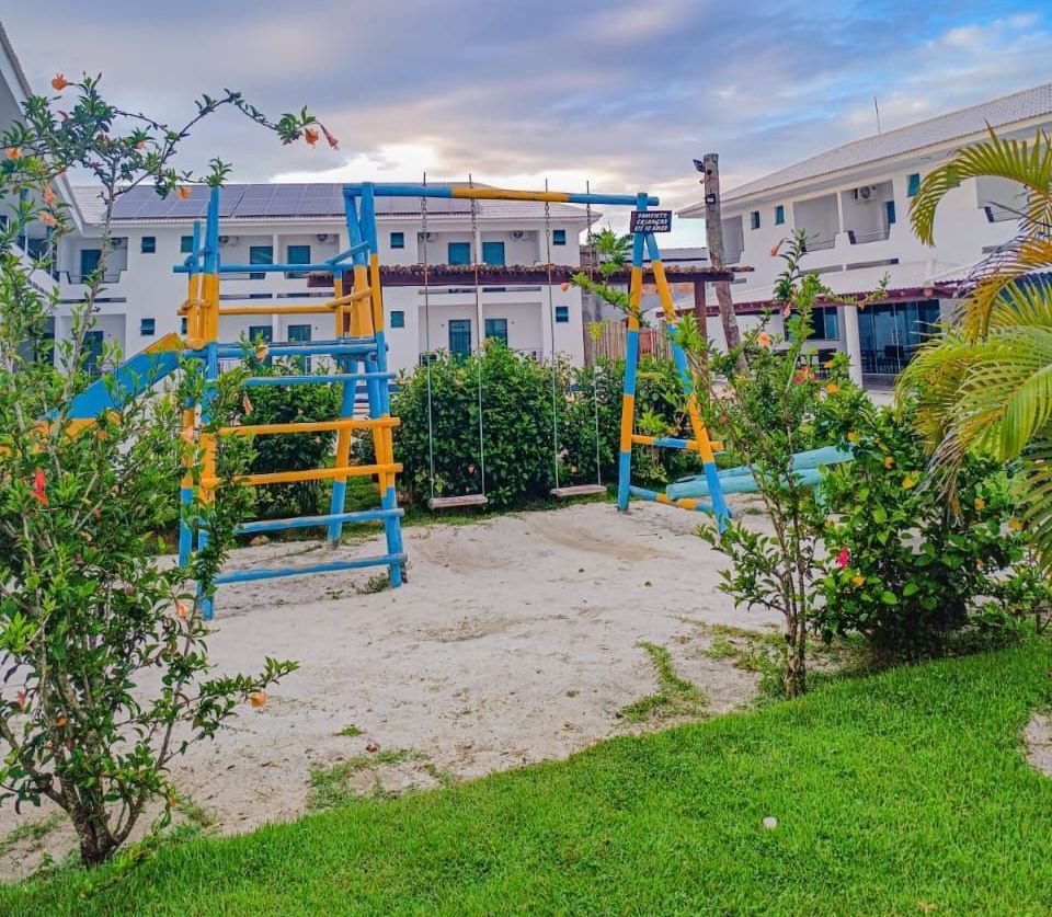 Um playground azul e amarelo em frente a um prédio branco Areia do Atlântico Hotel