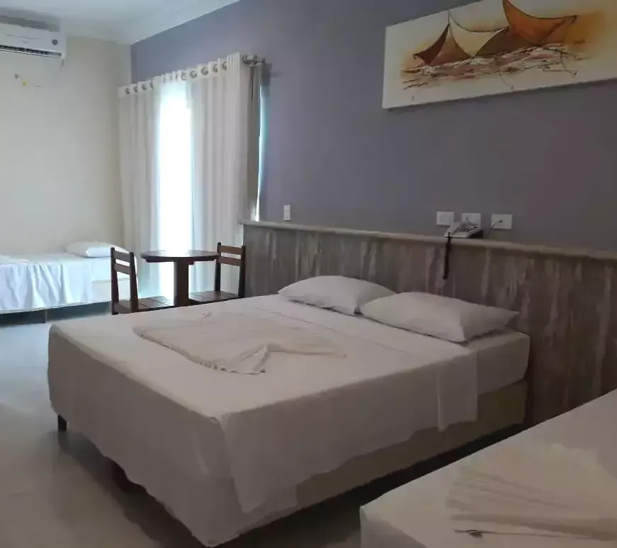 Um quarto de hotel com três camas e uma mesa Areia do Atlântico Hotel