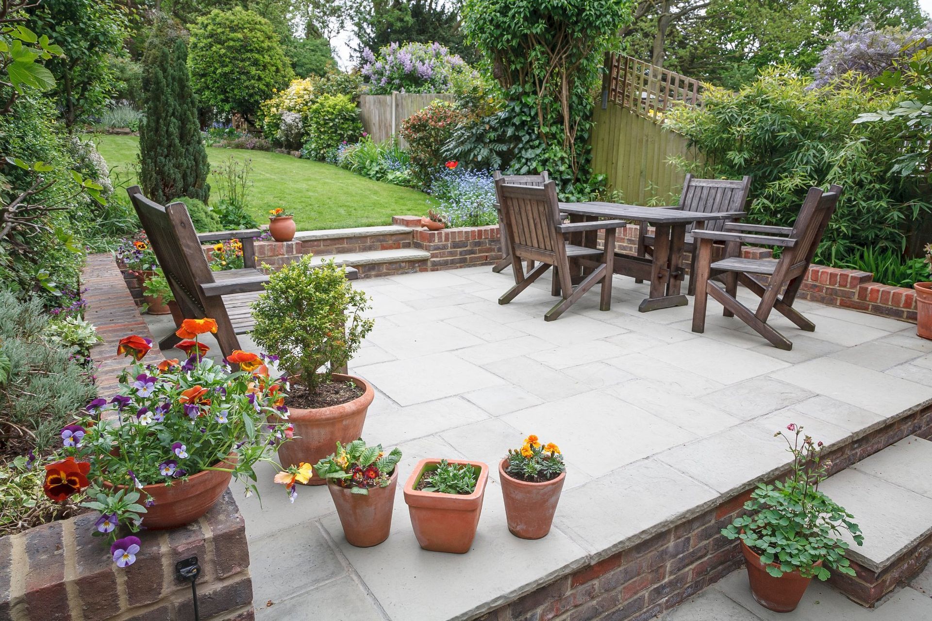 Patio garden with wooden table and chairs, potted flowers, and lush greenery