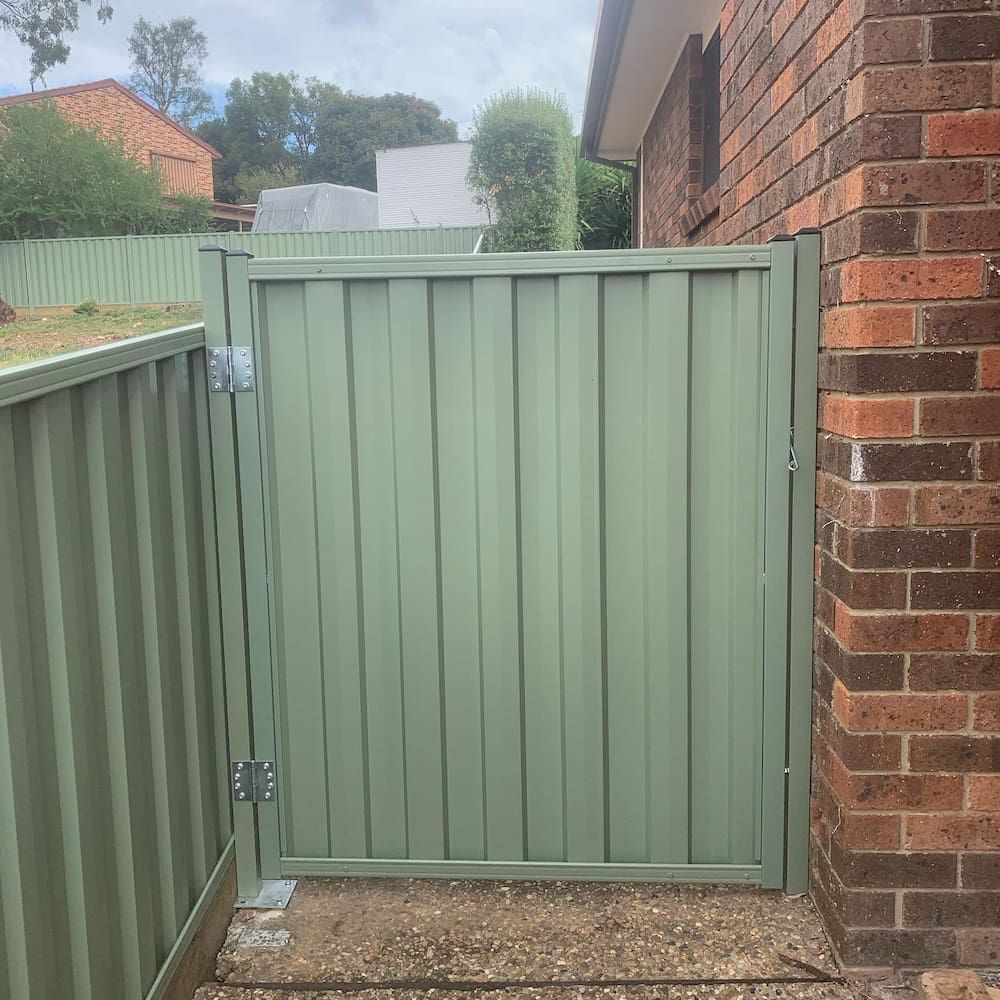 A Green Gate is Sitting Next to a Brick Wall — CLF Landscaping In Hawker, ACT