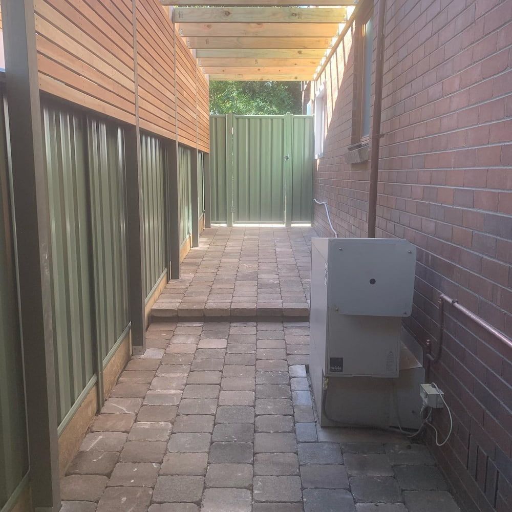 A Brick Walkway With a Green Fence in the Background — CLF Landscaping In Hawker, ACT