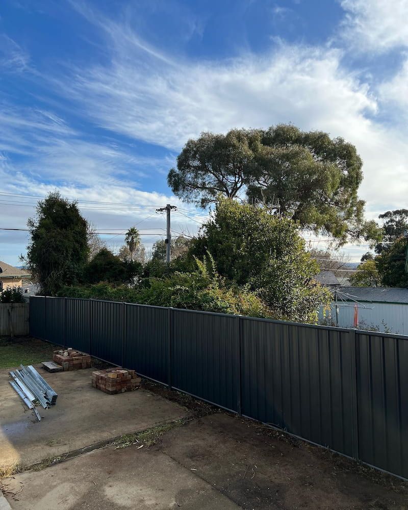 A Black Fence Surrounds a Backyard With Trees and a Blue Sky in the Background — CLF Landscaping In Hawker, ACT