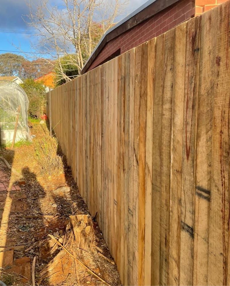 A Wooden Fence is Being Built Next to a Brick Building — CLF Landscaping In Hawker, ACT