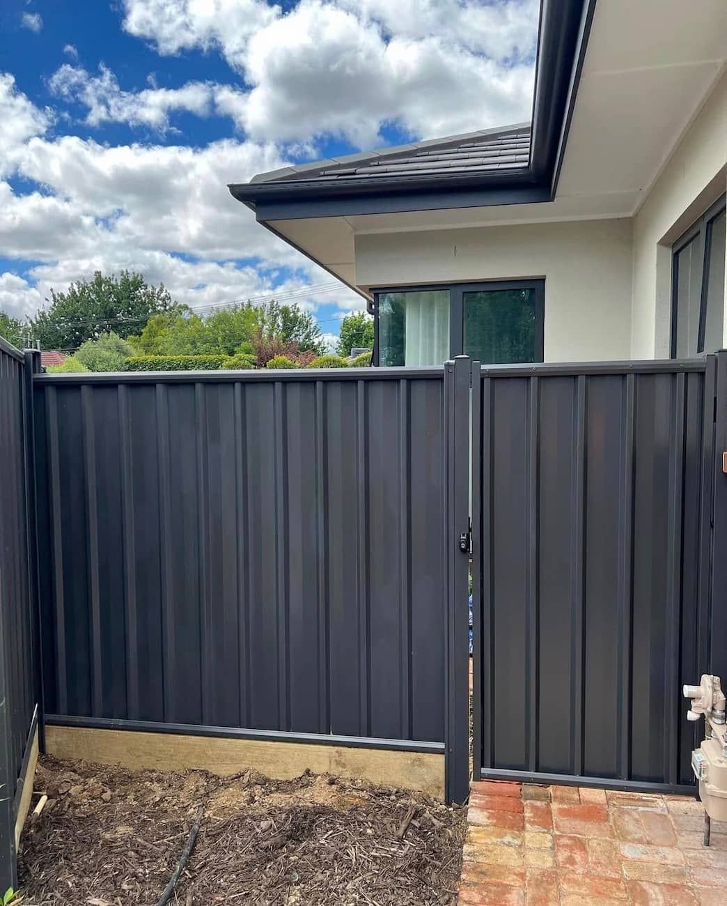 A Black Fence With a Gate in Front of a House — CLF Landscaping In Hawker, ACT