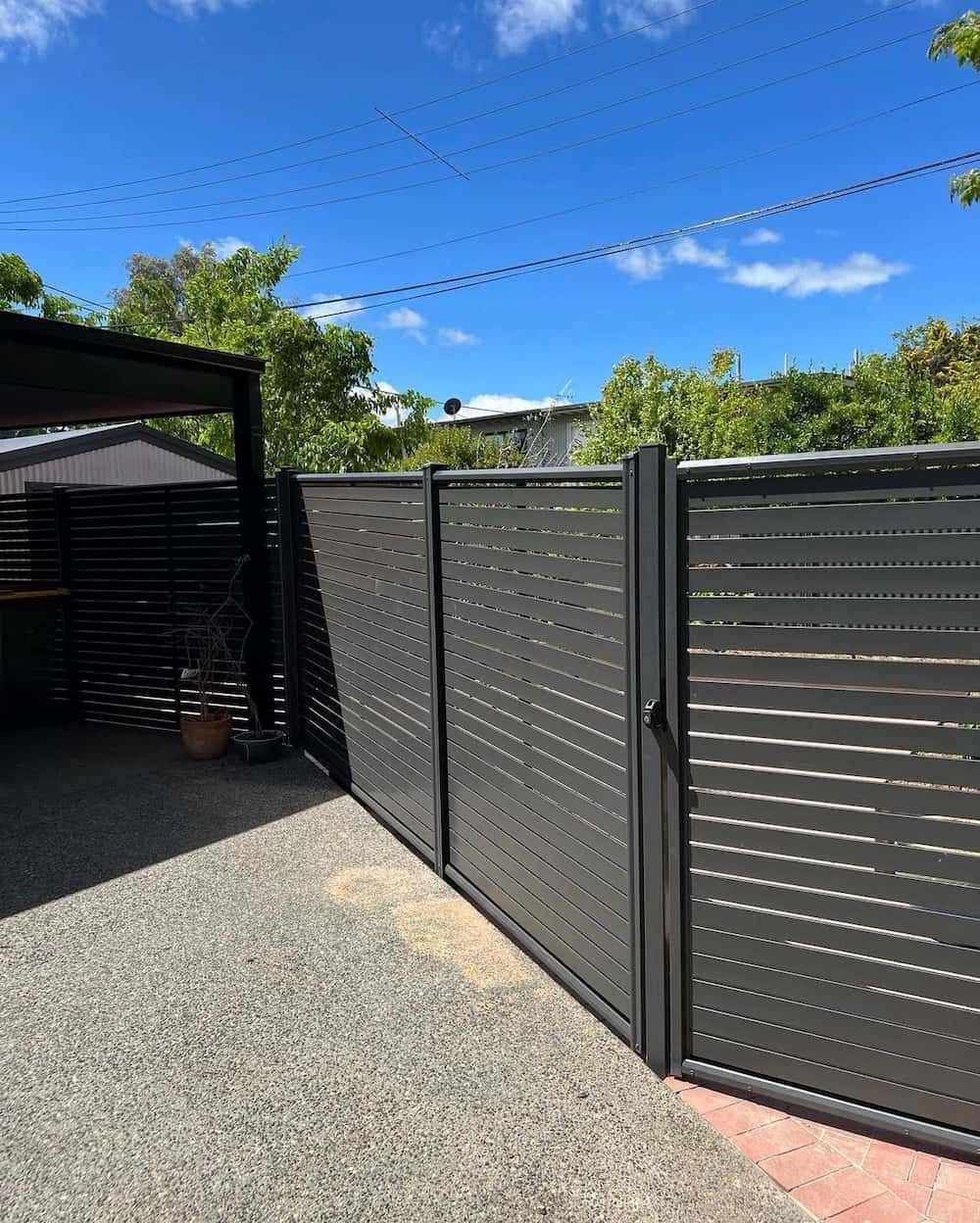 A Black Fence With a Gate in the Middle of a Driveway — CLF Landscaping In Hawker, ACT