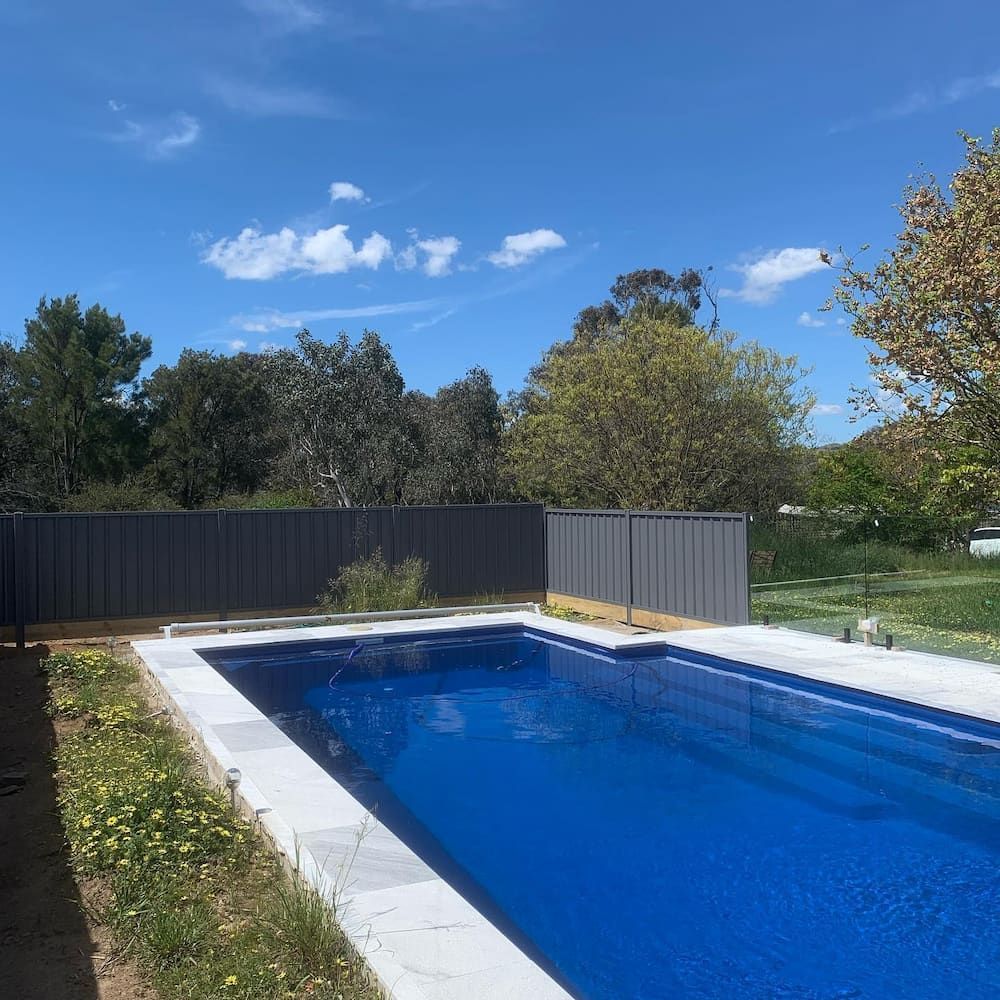 A Large Swimming Pool Surrounded by a Fence and Trees on a Sunny Day — CLF Landscaping In Hawker, ACT