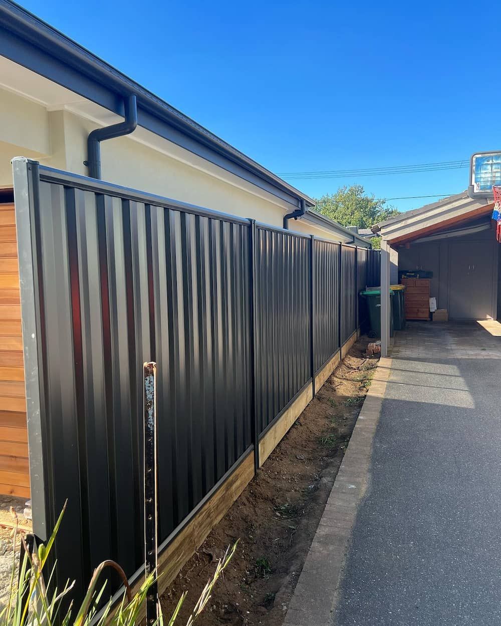 A Black Fence is Along the Side of a Road Next to a House — CLF Landscaping In Hawker, ACT