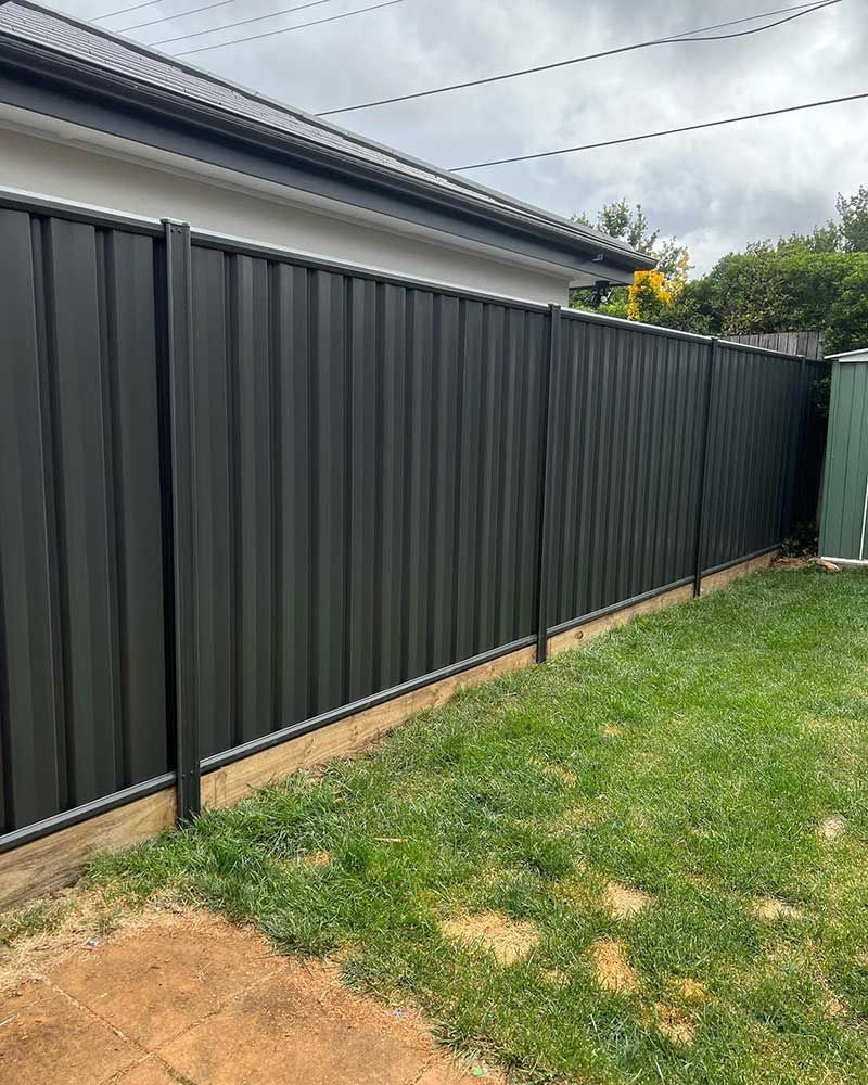 Black Corrugated Metal Fence Alongside a Grassy Yard, Bordering a Home With a Dark Roof — CLF Landscapes in Gungahlin, ACT