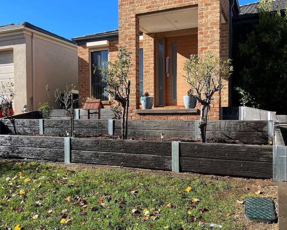 A Brick House With A Wooden Retaining Wall In Front Of It — CLF Landscaping In Hawker, ACT