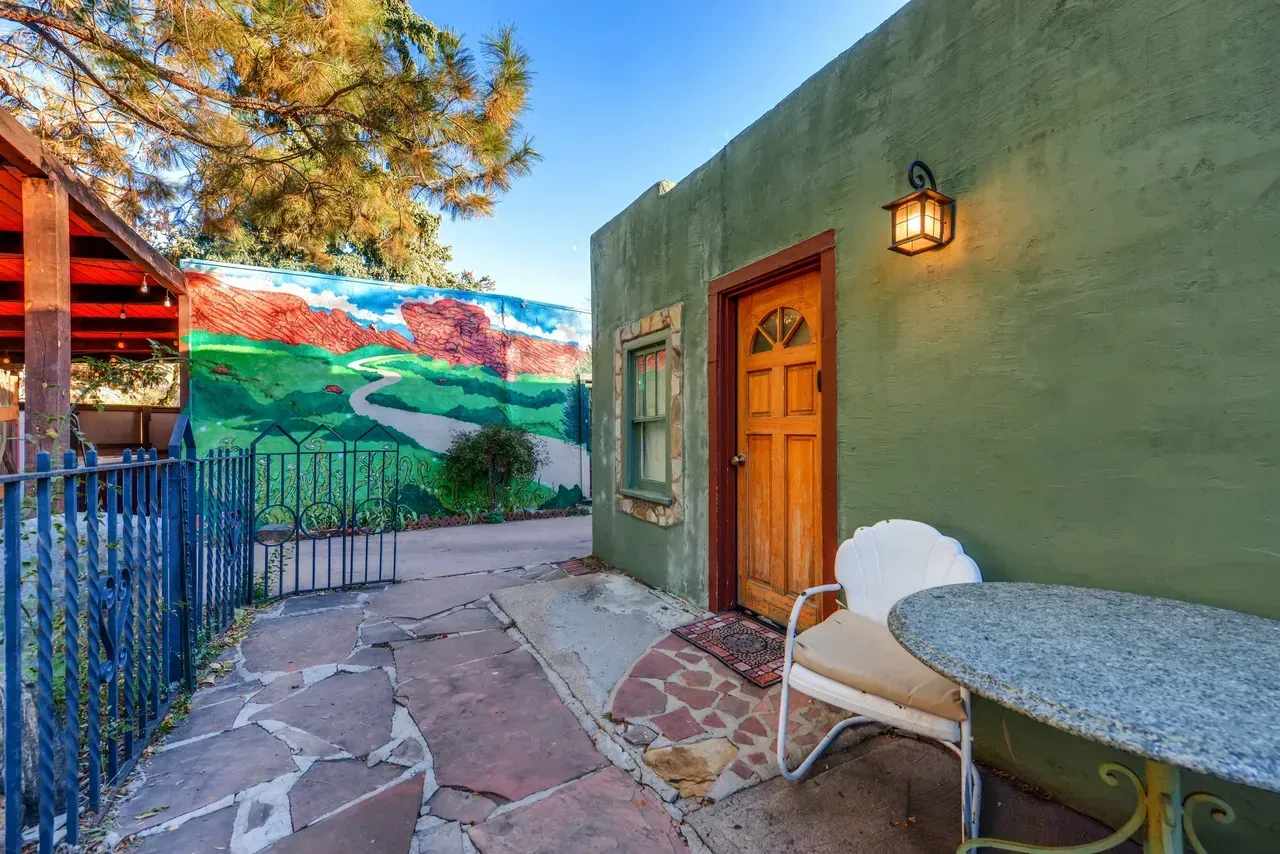 A patio area with stone flooring, a small bistro table, a white chair, a green building wall, and a painted landscape mural.