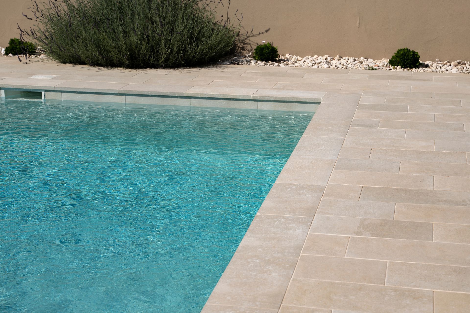 Vista de la piscina: baldosas de piedra clara que bordean una piscina turquesa.