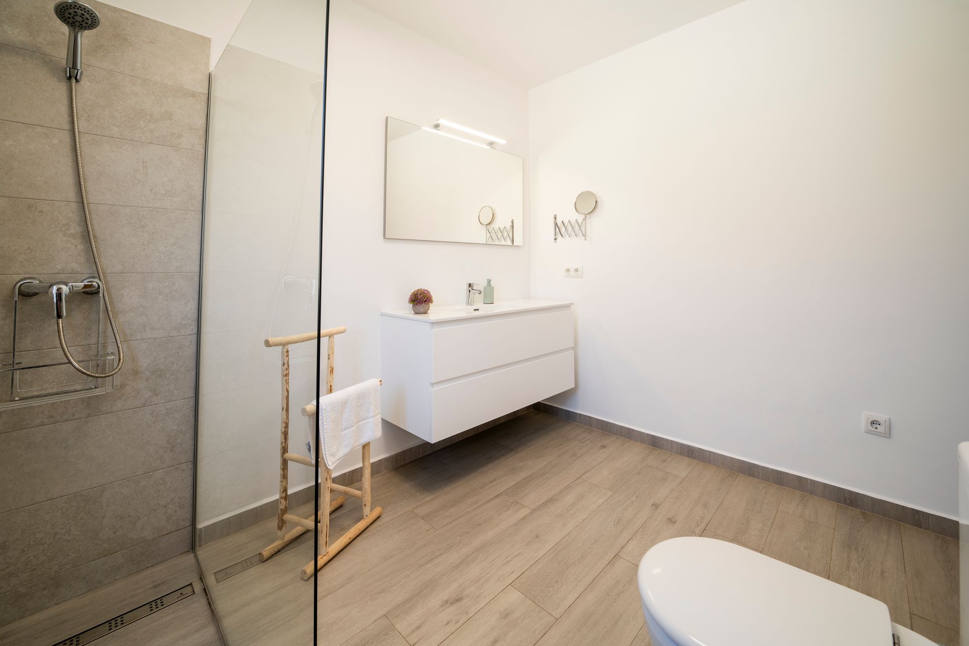 Baño moderno con ducha, tocador, inodoro y suelo de madera.