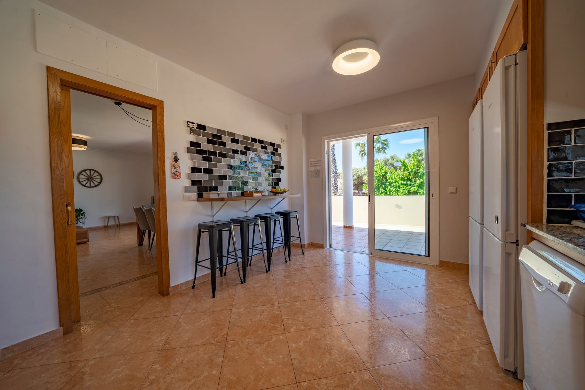 Cocina con piso de baldosas, taburetes en el mostrador, puerta corrediza al patio y puerta al comedor.