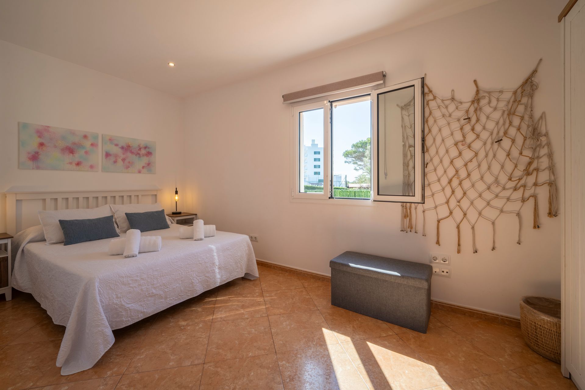 Dormitorio con cama de matrimonio, ventana, baúl de almacenaje y tapiz decorativo.