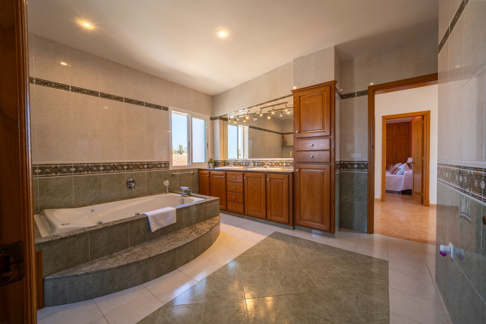 Amplio baño con jacuzzi, muebles de madera y puerta abierta a un dormitorio.