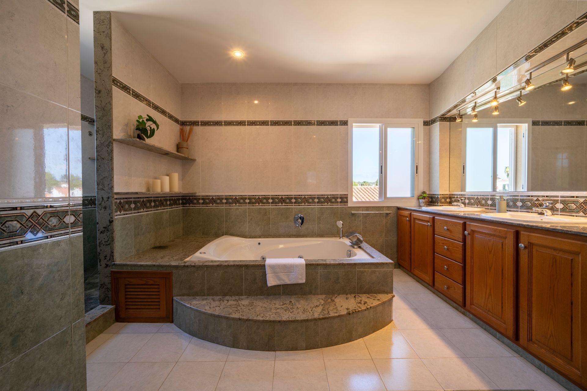 Amplio baño con bañera de hidromasaje y lavabo doble, en tonos beige y marrón, y ventanas.