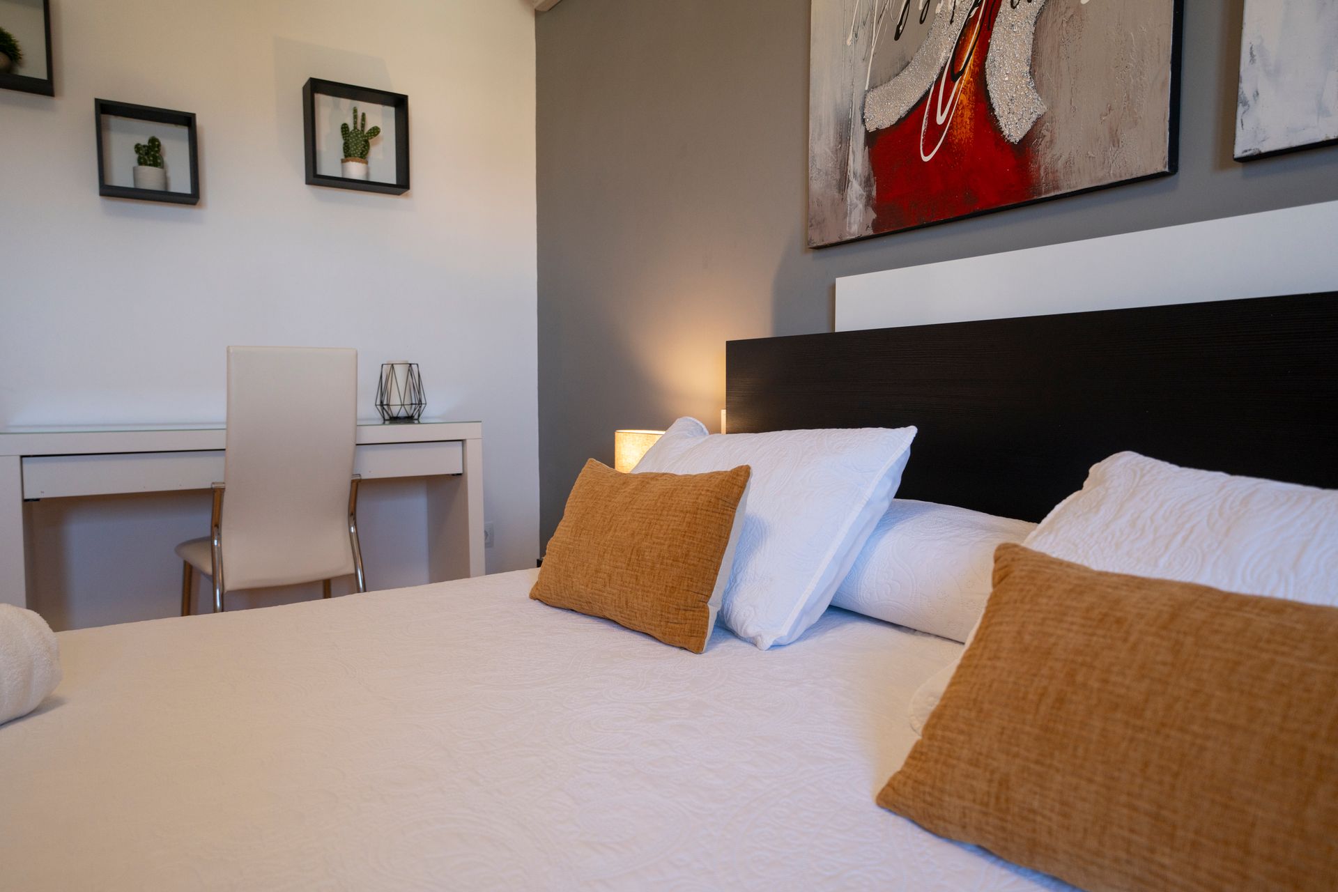 Dormitorio con cama, almohadas, escritorio y arte enmarcado en la pared.