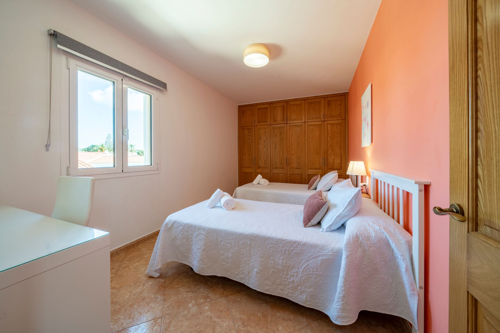 Dormitorio con dos camas blancas, ventana, pared color melocotón y armario de madera.