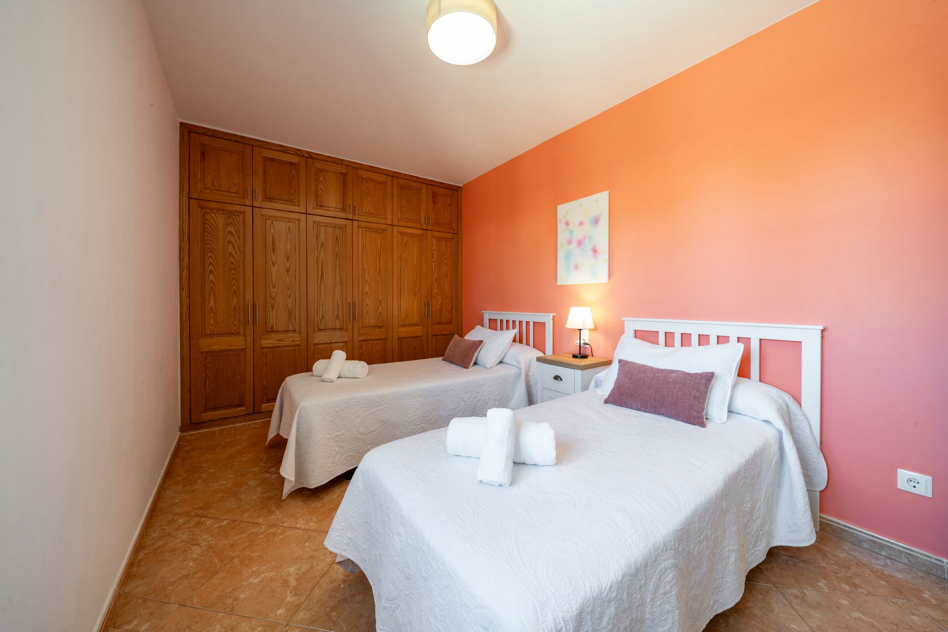Dormitorio con dos camas individuales, armario de madera y paredes color melocotón.