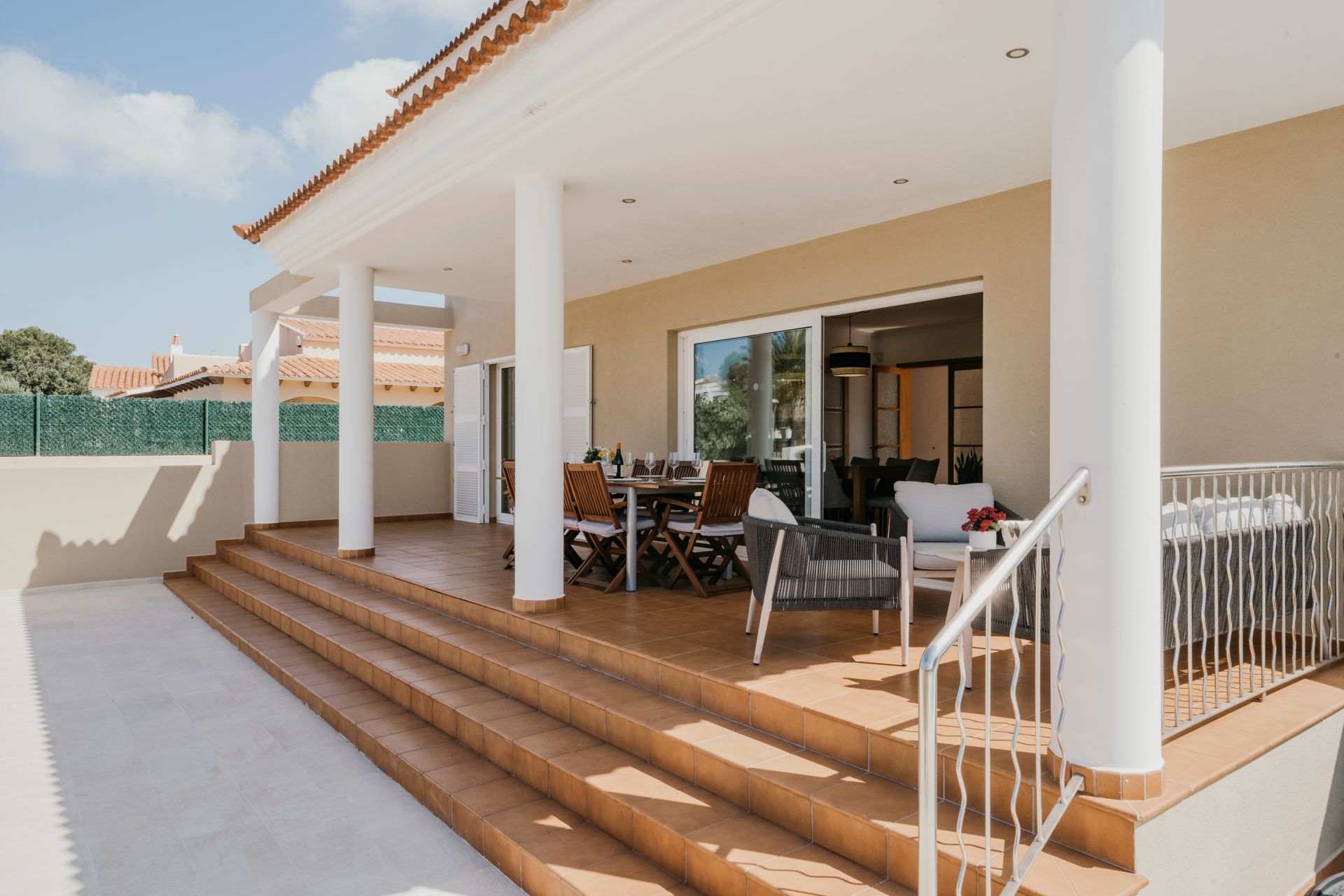Patio cubierto con asientos, mesa y escaleras que conducen a un área pavimentada; vista exterior.