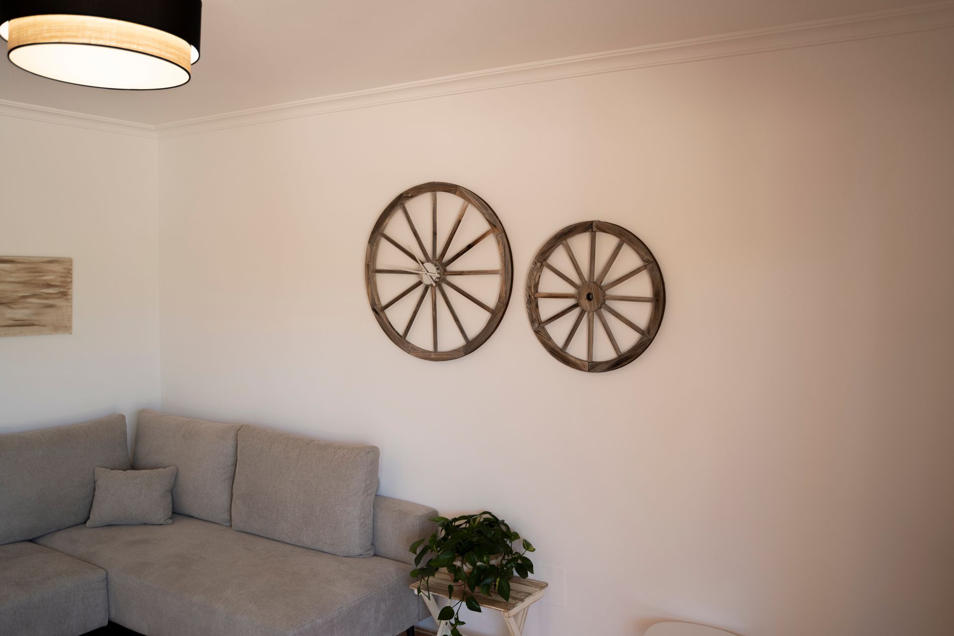 Sala de estar con dos ruedas de carro de madera sobre una pared blanca encima de un sofá gris y una pequeña planta.