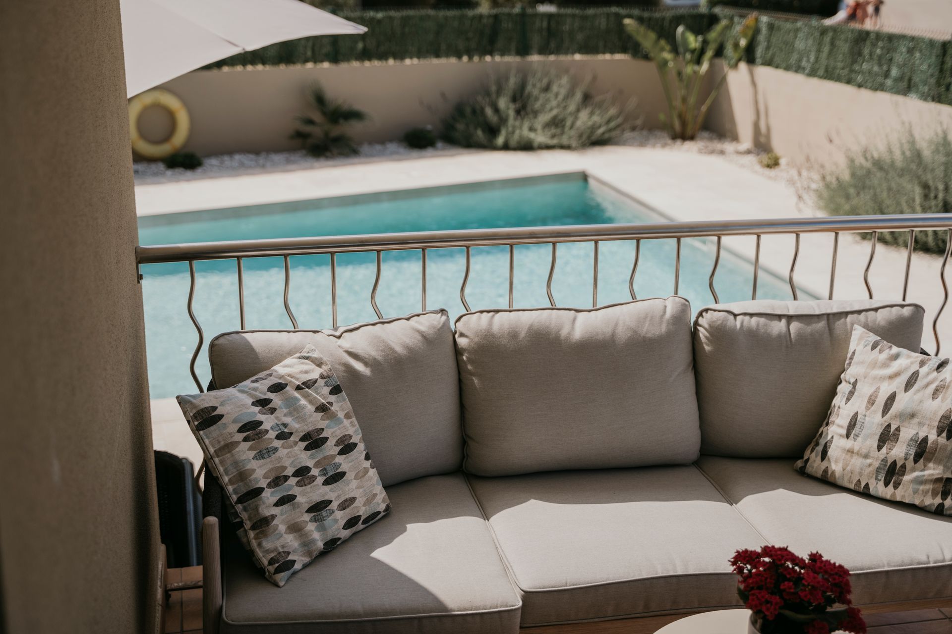 Balcón con sofá beige, almohadas y vista a la piscina.