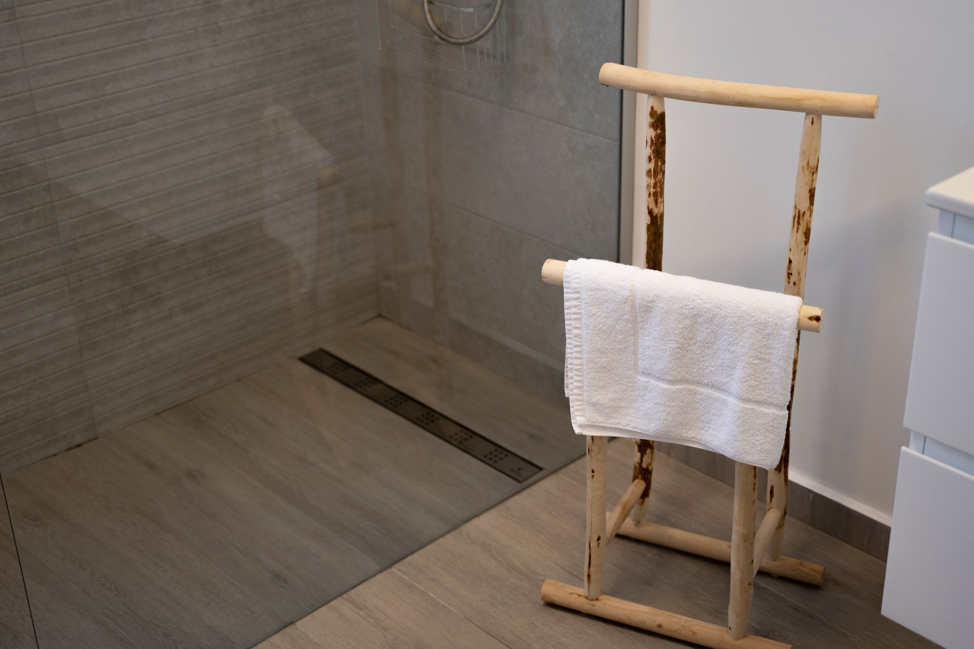 Un toallero de madera con una toalla blanca en un baño moderno con azulejos grises y ducha.