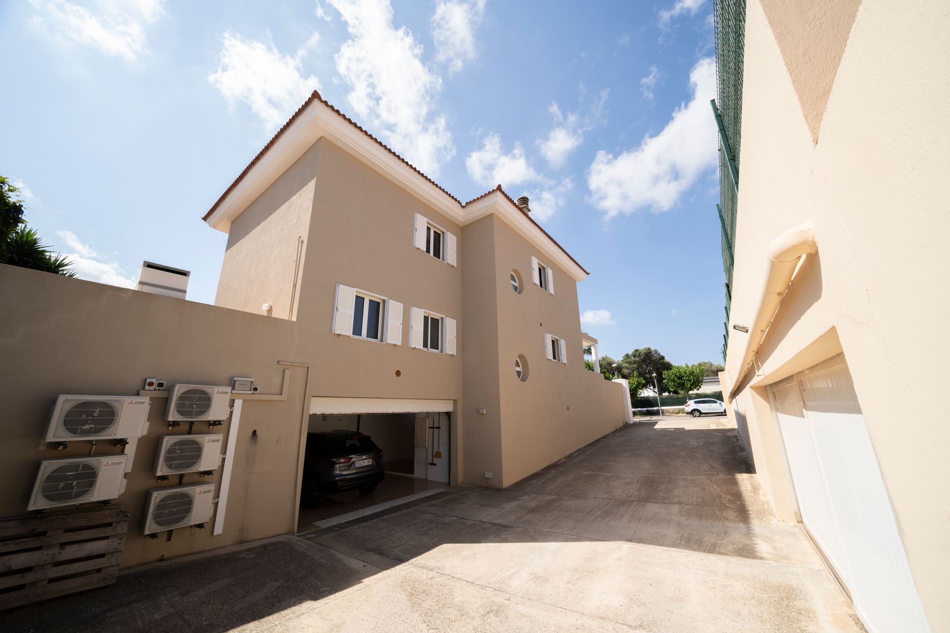 Casa de color canela con garaje y unidades de aire acondicionado, frente a un cielo azul con nubes.