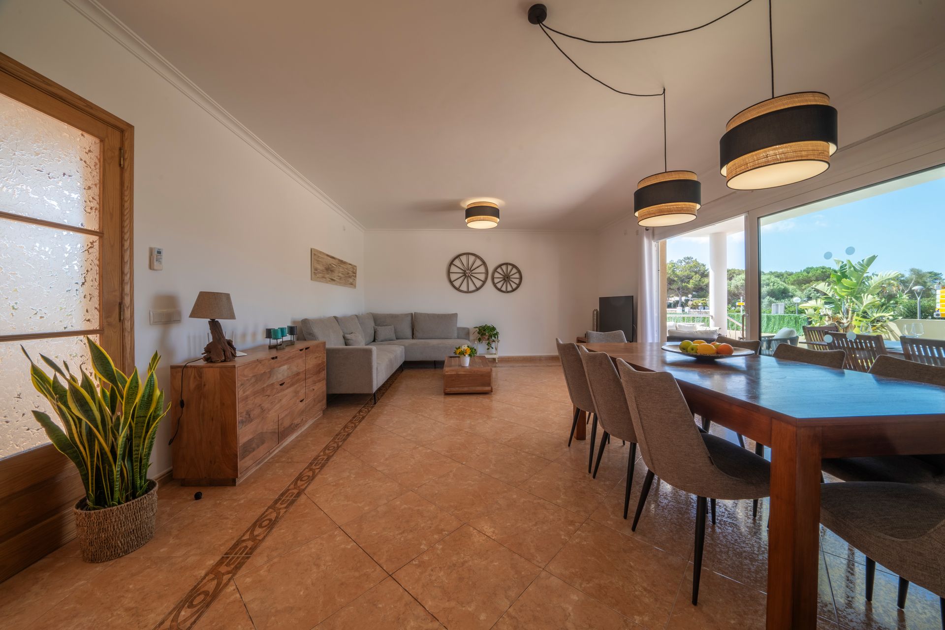 Amplia sala de estar y comedor con una mesa larga, un sofá seccional y grandes ventanales con vista a la vegetación.