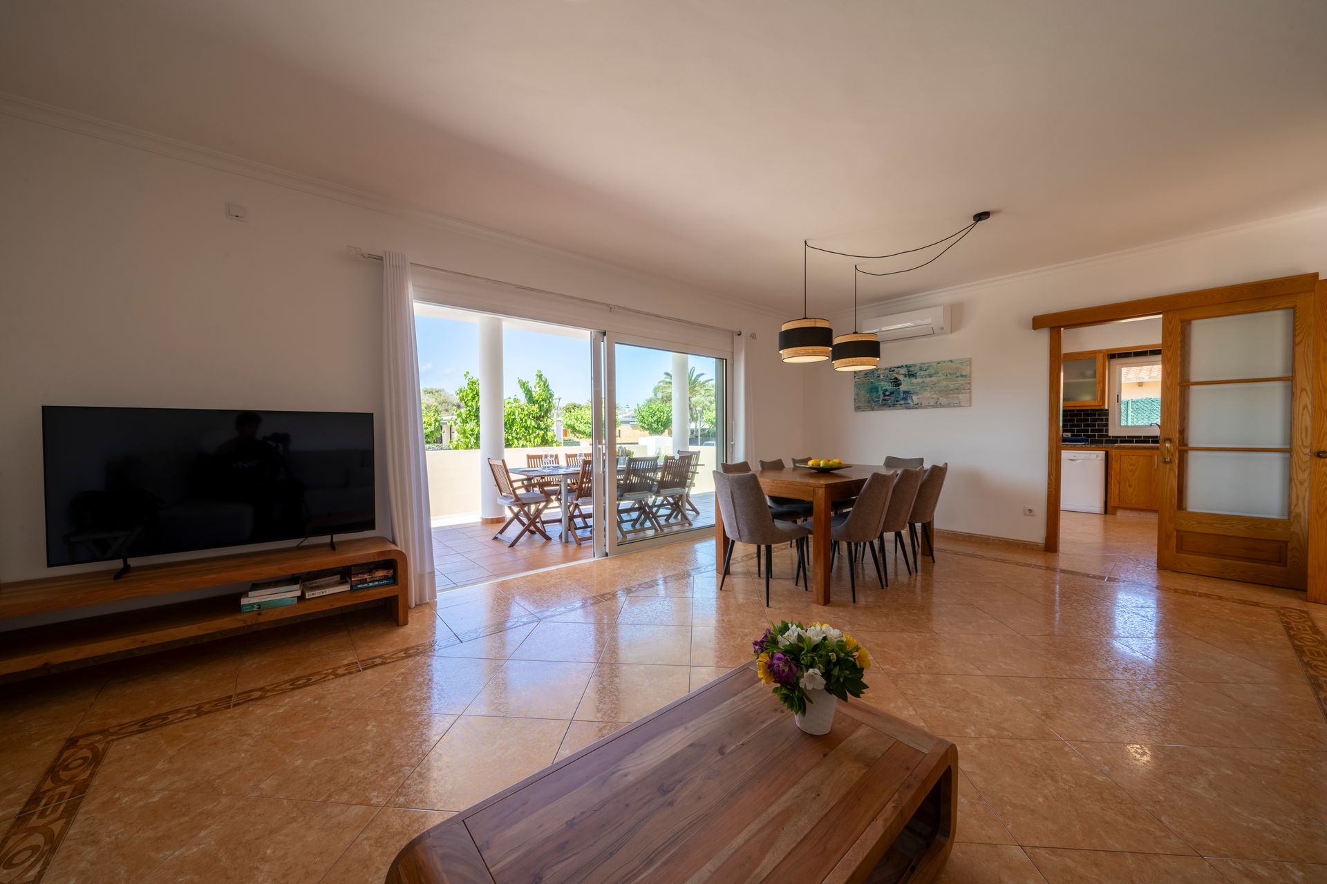 Amplia sala de estar con comedor, puertas corredizas de vidrio al patio, TV y entrada a la cocina.