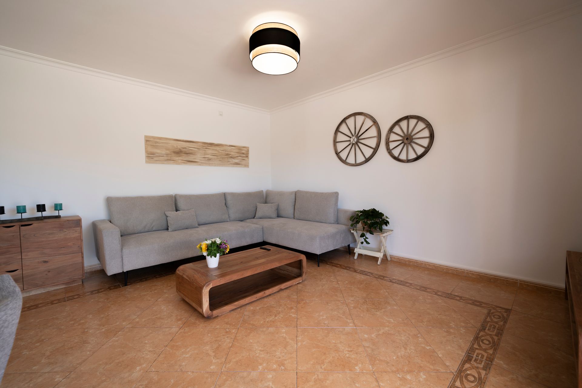 Sala de estar con sofá seccional beige, mesa de centro de madera y ruedas decorativas en la pared.