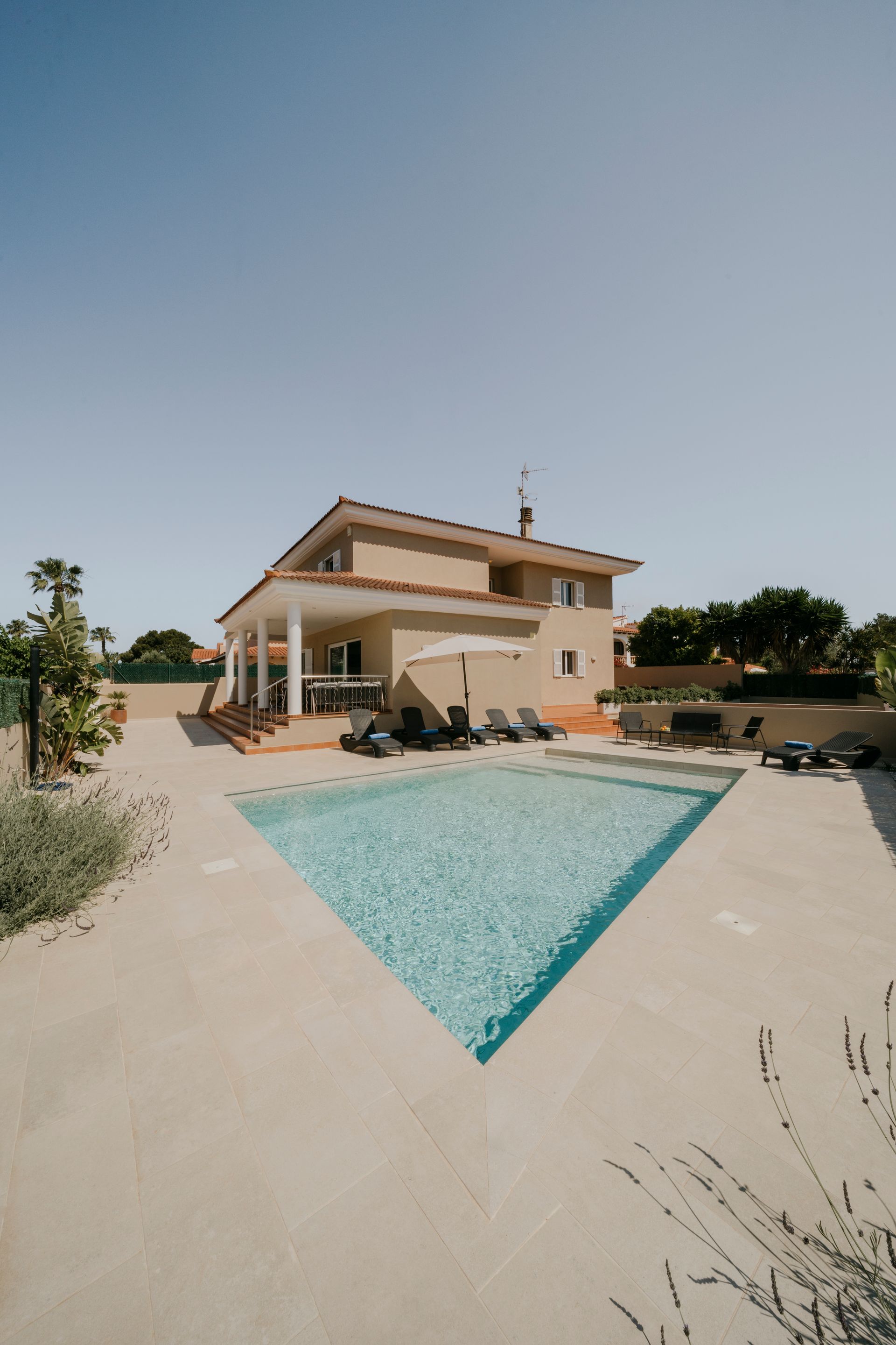Una casa beige de dos pisos con piscina en un día soleado.