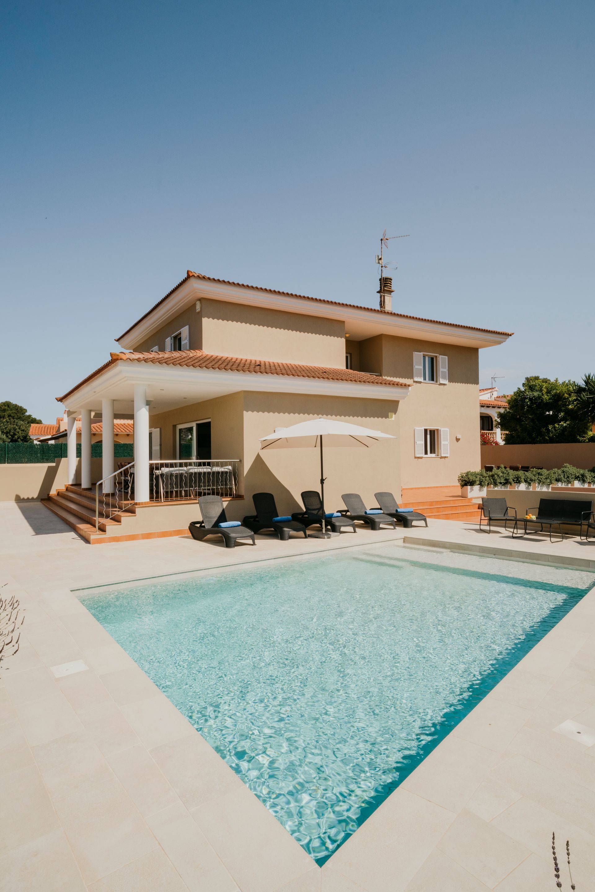 Casa de dos pisos con piscina y tumbonas en un día soleado.