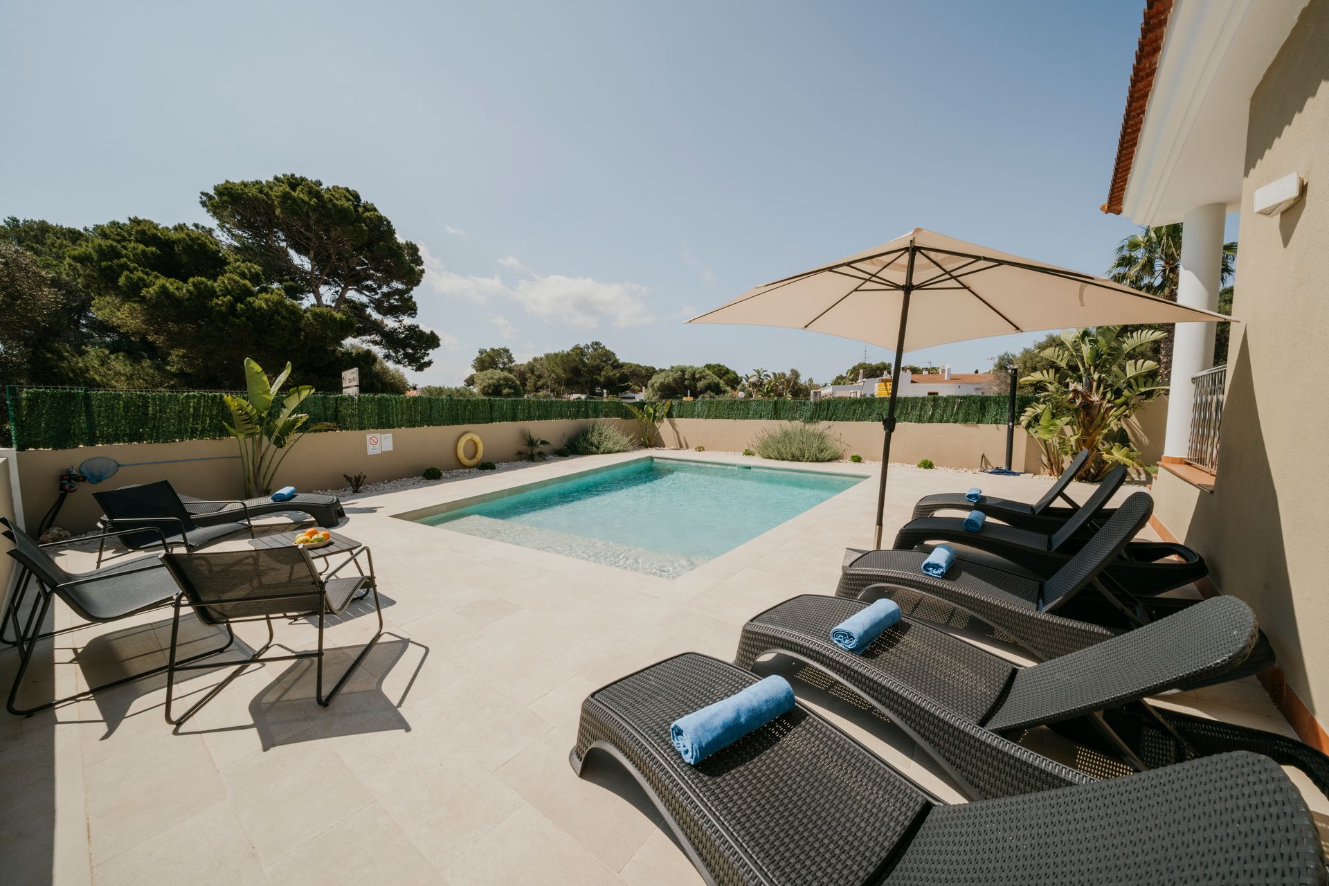 Patio junto a la piscina con tumbonas, piscina y sombrilla en un día soleado.