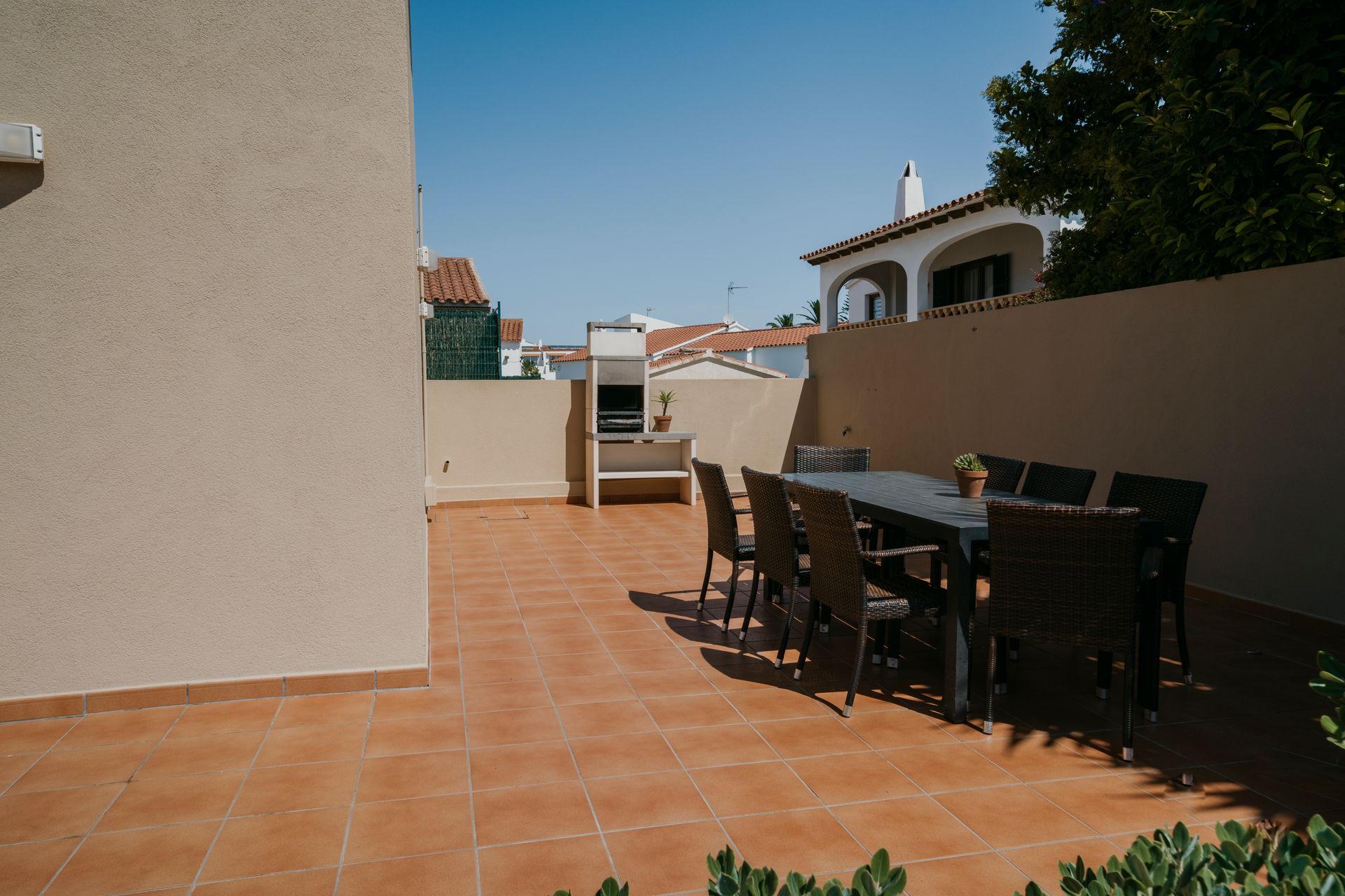 Patio con mesa y sillas, parrilla y paredes beige, con luz solar.