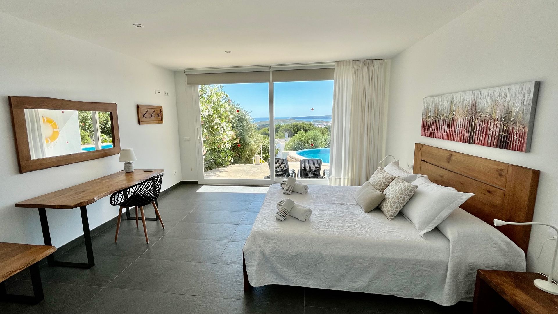 Dormitorio con cama, escritorio, puerta corrediza con vista a la piscina y al exterior.
