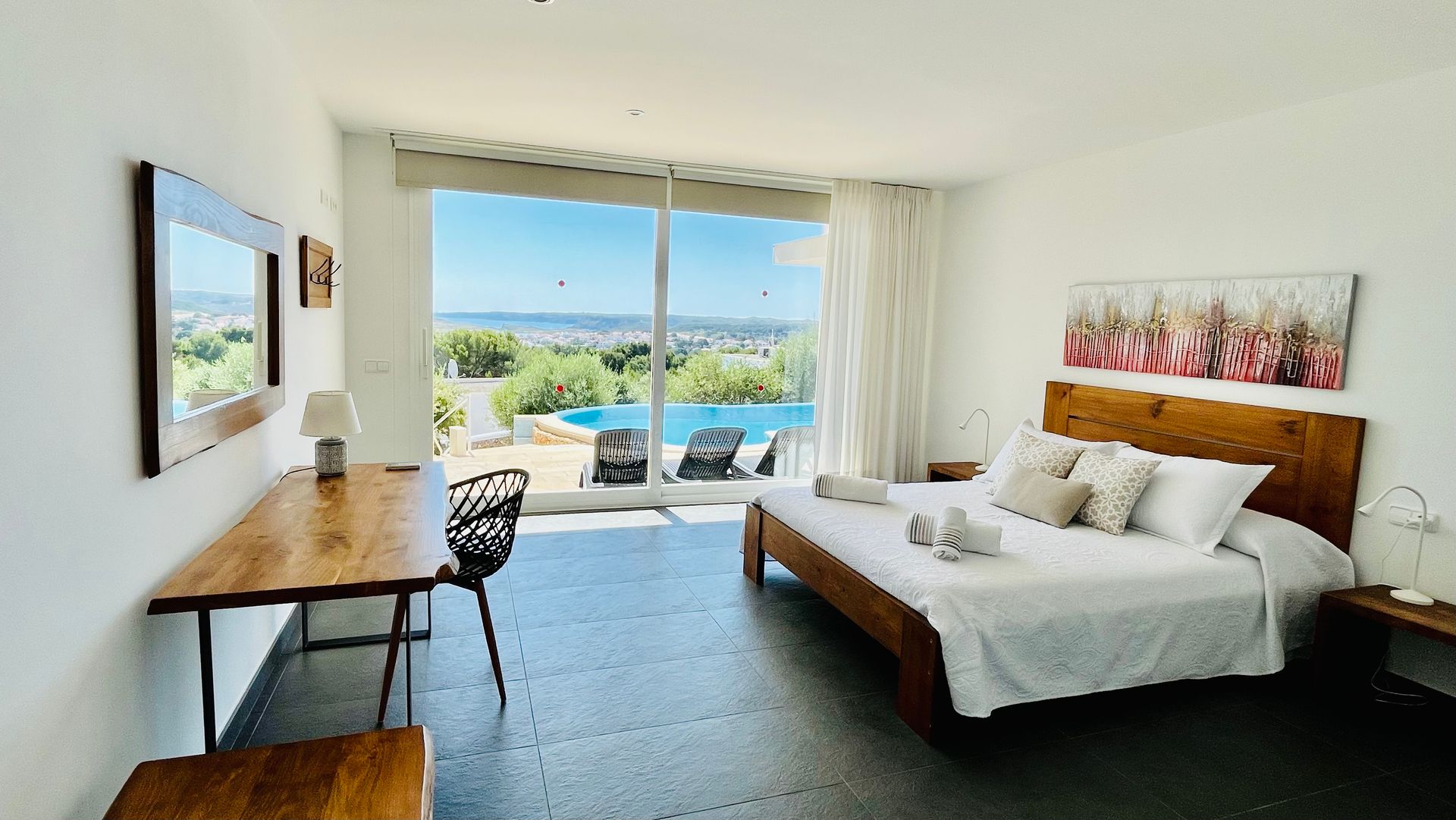 Dormitorio con cama, escritorio y gran ventanal con vista a la piscina y al paisaje.