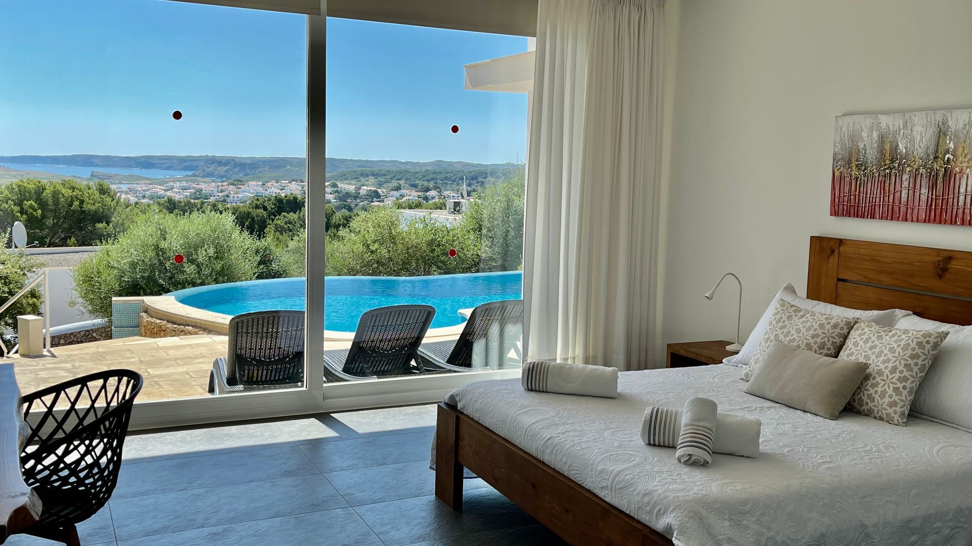 Dormitorio con vista a la piscina infinita con vista a una ciudad y al cielo azul.