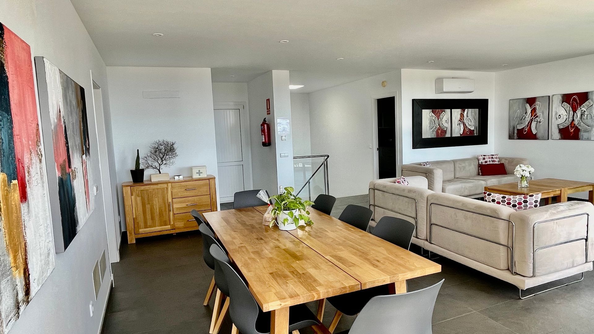 Amplio comedor y sala de estar con mesa de madera, sofá, obras de arte y escalera.